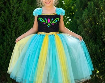 May include: A floor-length dress featuring a black crocheted bodice with a colorful pink, green, and yellow floral-inspired pattern. The skirt is made of layered light blue and yellow tulle, and the sleeves consist of small, ruffled blue tulle caps.