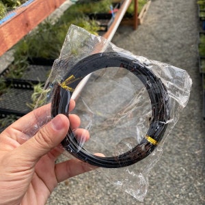 May include: A roll of black wire in a clear plastic bag. The wire is coiled into a circle and has a gold colored tie.