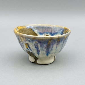 May include: A small, white ceramic bowl with a blue and gold glaze. The bowl has a rounded shape and a small foot.