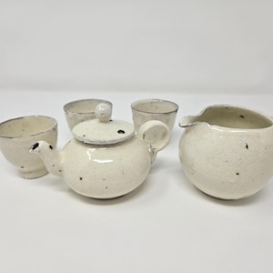 以下が含まれることがあります： 茶器セット。白い磁器製のティーポット、クリーマー、カップ3個。斑点模様の仕上げです。