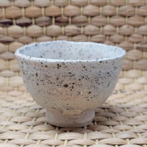 以下が含まれることがあります： 黒の斑点模様の白い陶器の小さなボウル。ボウルは丸みを帯びた形をしていて、小さな足がついています。