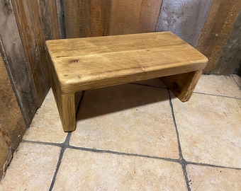 May include: A rustic wooden step stool with a natural wood finish. The stool is made of reclaimed wood and has a simple, functional design.