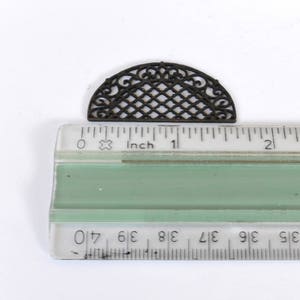 May include: A black metal decorative half-circle grate with a geometric design, measuring approximately 2.5 cm in diameter.