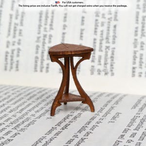 May include: A miniature brown wooden table with a triangular top and three curved legs. The table has a small shelf near the bottom. The table is set on a book.