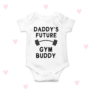 Pode incluir: Macacão branco para bebê com texto preto que diz "Daddy's Future Gym Buddy" com um gráfico de barra.