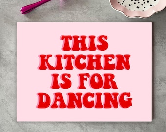 May include: Pink kitchen sign with the text "This Kitchen is for Dancing" in red retro-style lettering.