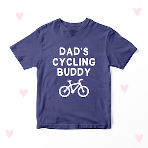 Op de afbeelding: Een marineblauw t-shirt met de witte tekst "DAD'S CYCLING BUDDY" en een witte fietsafbeelding. Het shirt heeft een ronde hals en is waarschijnlijk gemaakt van katoen of een vergelijkbare stof.