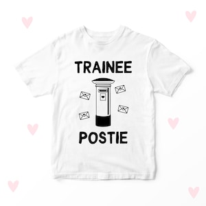 May include: White t-shirt with black text that says "Trainee Postie" and a black illustration of a post box with envelopes.
