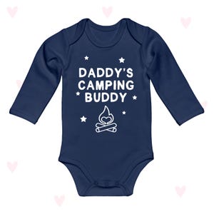 Op de afbeelding: Marineblau baby-rompertje met lange mouwen. De witte tekst luidt "DADDY'S CAMPING BUDDY" met steraccenten en een kampvuurafbeelding. Een schattige outfit voor een baby.