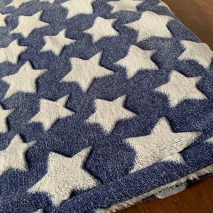 May include: A blue and white textile featuring a repeating pattern of white stars. The stars are raised, creating a textured effect against the blue background. The fabric appears soft and plush.