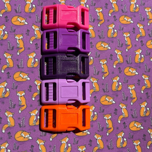 May include: Five plastic slider buckles in different colors: pink, purple, dark purple, light purple, and orange. The buckles are stacked on top of each other.