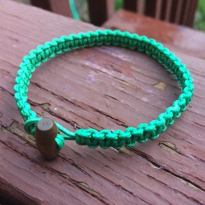 Peut inclure: Un bracelet en paracorde vert avec un fermoir en laiton en forme de balle.