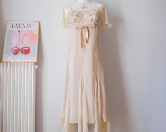 May include: A cream-colored midi dress featuring short flutter sleeves, a square neckline, and a bodice adorned with intricate silver and gold beadwork. A satin ribbon tie sits at the waist, while the skirt has a handkerchief hemline.