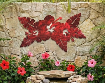 May include: A decorative metal wall art piece featuring red hibiscus flowers and leaves is mounted on a stone wall. The wall is part of a garden scene with a small waterfall, pond, and vibrant red and pink hibiscus flowers.