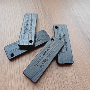 Könnte beinhalten: Vier schwarze Holzetiketten mit graviertem Text. Die Etiketten sind rechteckig und haben abgerundete Ecken. Der Text auf den Etiketten lautet "Antique Bog Oak 1270-6450 years old" und "Antique Bog Oak 1270-64 years old".