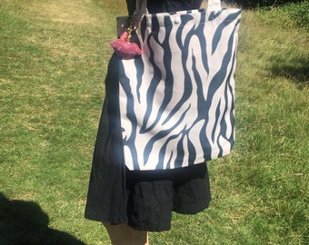 May include: A white and black zebra print tote bag with a pink lip keychain. The bag has a long strap and is made of canvas.