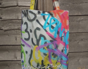 May include: A white canvas tote bag with colorful graffiti-style designs and the text "Unravelling Minds".