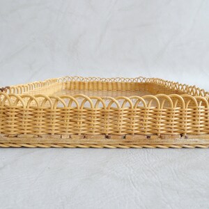 May include: A woven wicker tray with a decorative scalloped edge. The tray is made of natural light brown wicker and has a rectangular shape.