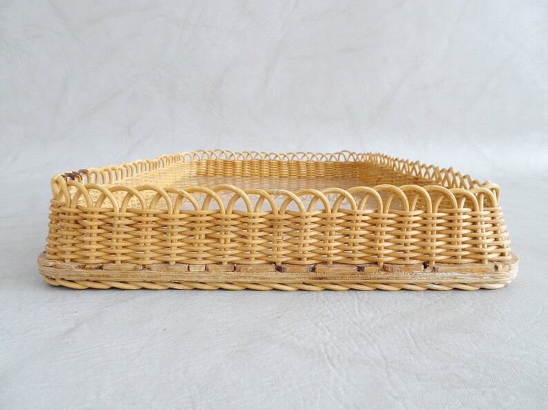 May include: A woven wicker tray with a decorative scalloped edge. The tray is made of natural light brown wicker and has a rectangular shape.