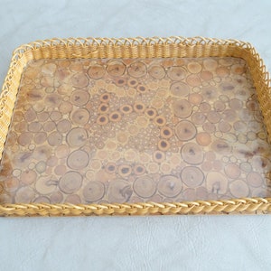 May include: A rectangular tray with a woven wicker border and a clear top. The tray's surface is made of a unique material that resembles a mosaic of wood slices.
