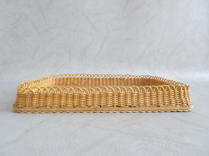 May include: A rectangular woven wicker tray with a decorative scalloped edge. The tray is made of natural light brown wicker.