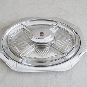 Könnte beinhalten: Ein silbernes Serviertablett mit einem Glaseinsatz, der in vier Abschnitte unterteilt ist. Das Tablett hat ein geometrisches Design und eine erhöhte Mitte.