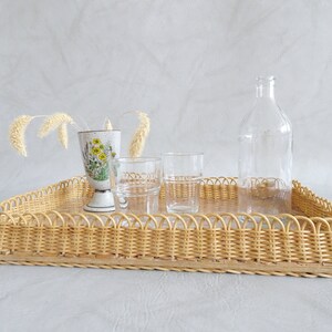 May include: A wicker tray with a decorative floral design vase, two clear glass cups, and a clear glass bottle.