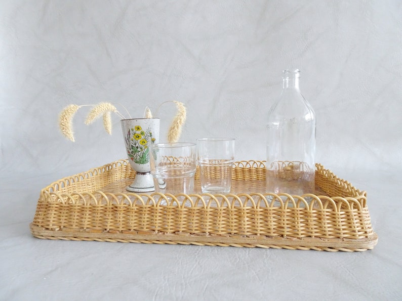 May include: A wicker tray with a decorative floral design vase, two clear glass cups, and a clear glass bottle.