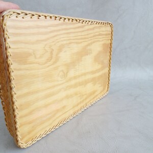 May include: A rectangular wooden tray with a woven wicker border. The tray is made of light wood and has a natural finish.