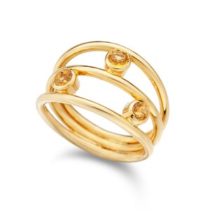 May include: A gold ring with three small, round, yellow gemstones set in a triple band design.