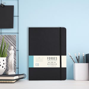 Puede incluir: Un cuaderno negro con cierre elástico negro y una etiqueta blanca que dice "FORBES square 240 ruled NOTEBOOK HAMMOND STATIONERY CO. LTD. F20".