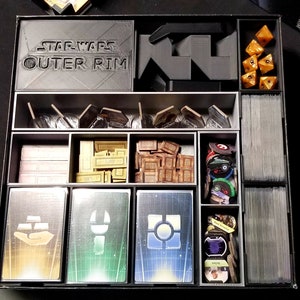 May include: A black organizer with the words "Star Wars Outer Rim" on the front. The organizer has compartments for storing game pieces, cards, and dice. The organizer is made of plastic and has a black finish.