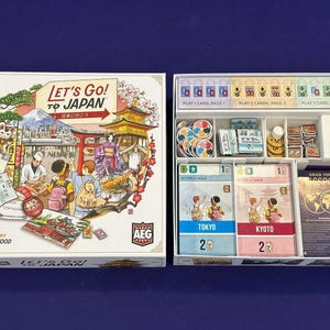 Puede incluir: Juego de mesa "Let's Go! To Japan" con ilustraciones de monumentos y personas japonesas. La caja del juego está abierta, revelando componentes, cartas y fichas. El juego incluye cartas para Tokio y Kioto.