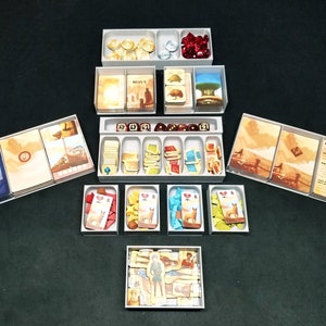 Può includere: Un set di scatole di stoccaggio in plastica trasparente per organizzare un gioco da tavolo. Le scatole contengono vari componenti del gioco, tra cui carte, dadi e gettoni. Le scatole sono etichettate con i nomi dei componenti del gioco.
