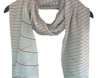 May include: A light blue and grey striped scarf with a subtle ombre effect. The scarf has a fringed edge and is made of a soft, lightweight fabric.
