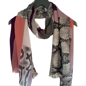May include: A multi-coloured scarf with a snakeskin pattern. The scarf is made of a soft, lightweight fabric and features shades of pink, purple, grey, and white.