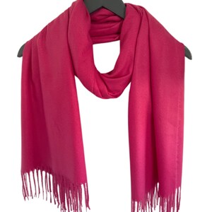 May include: A bright pink scarf with fringe on the ends. The scarf is made of a soft, lightweight material.