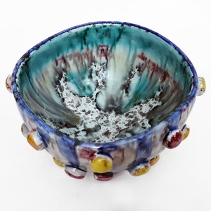 Peut inclure: Un petit bol en céramique bleu et blanc avec un glaçage moucheté coloré. Le bol a une forme arrondie et est décoré de petits points colorés autour du bord.