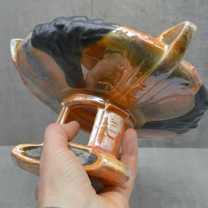 May include: A ceramic bowl with a stand. The bowl is orange, black, and brown with a glossy finish. The stand is orange and has a square base.