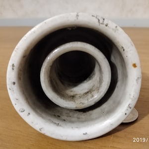 以下が含まれることがあります： 白磁製の絶縁体で、大きな丸い開口部と、その中に小さな丸い開口部があります。絶縁体はわずかにざらざらした表面をしていて、電気配線に使用されているようです。