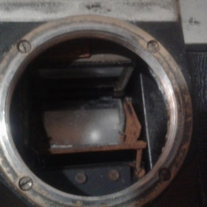 Puede incluir: Vista cercana del interior de una c&aacute;mara vintage. El visor es visible, con una pantalla de vidrio esmerilado y un marco de metal. El cuerpo de la c&aacute;mara est&aacute; hecho de metal negro con un borde plateado.