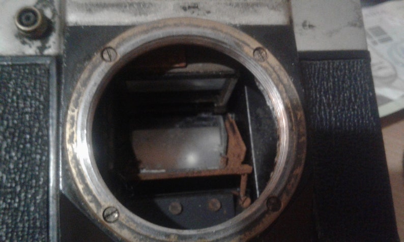 Puede incluir: Vista cercana del interior de una c&aacute;mara vintage. El visor es visible, con una pantalla de vidrio esmerilado y un marco de metal. El cuerpo de la c&aacute;mara est&aacute; hecho de metal negro con un borde plateado.