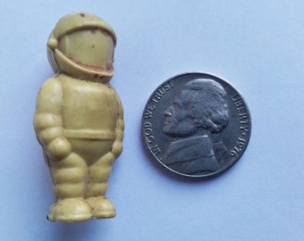 Könnte beinhalten: Eine gelbe Plastikfigur eines Astronauten, die aufrecht steht, mit einem Helm und einem detaillierten Raumanzug. Die Figur ist etwa so groß wie eine deutsche Fünf-Cent-Münze.