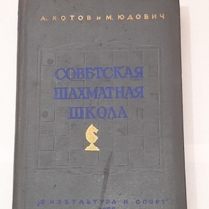 Op de afbeelding: Een grijs boek met de titel "Soviet Chess School" in blauwe letters. De omslag van het boek toont een schaakbord met een gouden schaakpaard in het midden. Het boek is in 1955 uitgegeven door "Fizkultura i Sport".