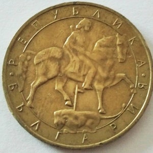 May include: A gold-colored coin with the inscription "REPUBLIKA  SLOVAKIA" around the edge. The center of the coin features a depiction of a knight on horseback, with a lion lying beneath the horse.
