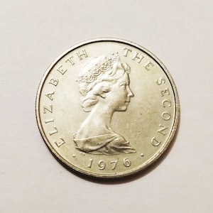 Puede incluir: Moneda plateada con el perfil de una mujer coronada, con la inscripción "ELIZABETH THE SECOND". El año "1976" también es visible. Un objeto de colección.