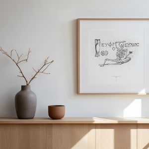 Può includere: Una stampa d'arte quadrata incorniciata con un'illustrazione a inchiostro nero di uno scheletro reclinato con il testo greco EΥΦΡΟΣΥΝΟΣ, accompagnata da un vaso grigio con rami spogli e una piccola ciotola marrone su un mobile in legno chiaro.