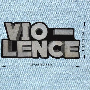 Op de afbeelding: Een grijze patch met het woord "VIOLENCE" in 3D-blokletters, omrand met zwart. De patch is 25 cm breed en 11,5 cm hoog. De patch bevindt zich op een lichtblauwe denim achtergrond.