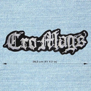 Könnte beinhalten: Schwarz-weißer, gestickter Aufnäher mit dem Text "Cro-Mags" in gotischer Schrift. Der Aufnäher ist etwa 29,5 cm lang. Der Aufnäher befindet sich auf einem hellblauen Jeansstoff-Hintergrund.