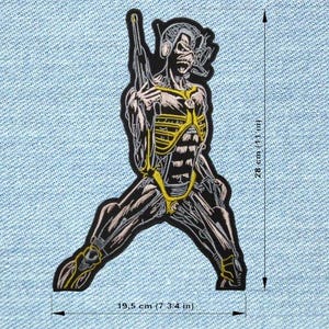 May include: A black, white, and yellow patch depicting a skeletal figure with a weapon, measuring 19.5 cm wide and 28 cm tall. The figure is detailed with muscle and bone structure, set against a light blue denim background. The patch is an Iron Maiden design.